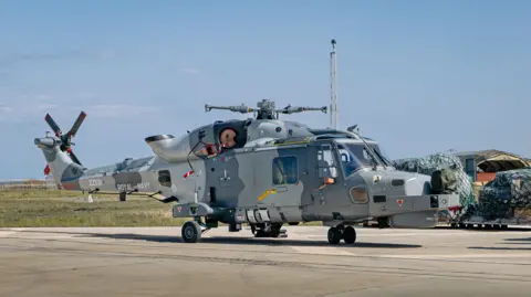 The Royal Navy Merlin Mk2 helicopter on the runway at RAF Akrotiri in Cyprus after it arrived following its journey from Cornwall. It is on a concrete runway on a bright sunny day. 