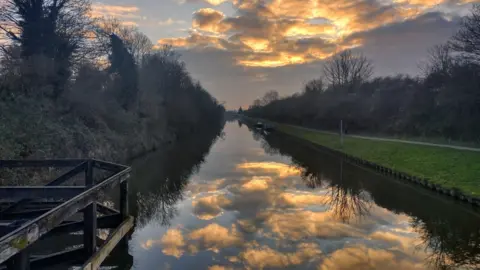 Tone Poet A group of clouds reflecting in the river at Quedgeley. The water is calm and along both sides there is grass and trees