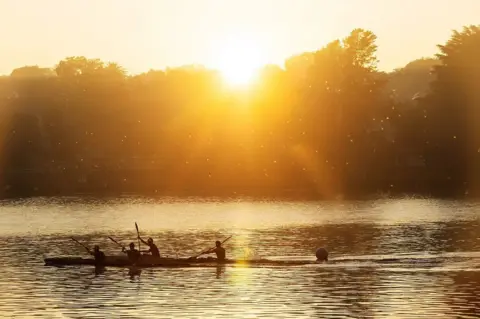 Kim Ludbrook / EPA The silhouettes of people in canoes paddle in the low, orange glow of the rising sun.