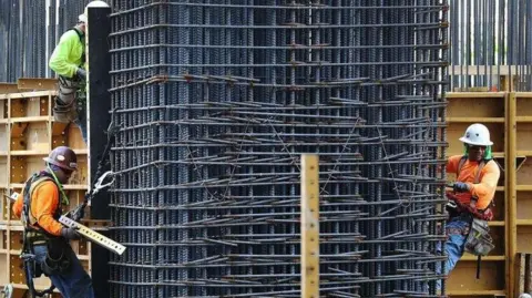 Three construction workers are attached to the building they are working on via harnesses