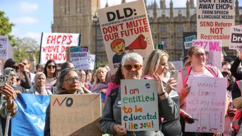 Getty Images People are standing outside Westminster on a sunny day with placards protesting. They are holding signs regarding Send such as "I am entitled to be educated like you" and "I want to learn with my friends and you can help"