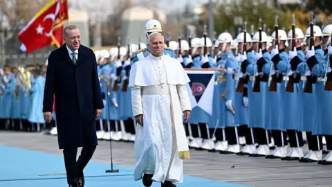 Anadolu via Getty Images Turkish President Recep Tayyip Erdogan (L) welcomes Pope Leo XIV (R) with official ceremony as they walk past soldiers in blue uniforms on a blue carpet