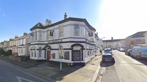 Google Maps A white building with black horizontal stripes painted across it. The Grenville is painted in black lettering. The building is two storeys.