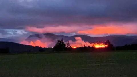 Fire on a hillside at night. The whole area is lit up in orange and pink 