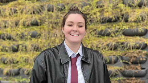 Young woman in shirt and leather jacket with a red tie.