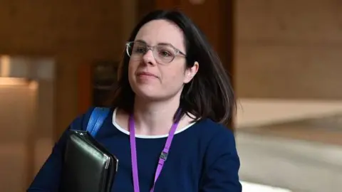 Getty Images Kate Forbes, with dark hair and glasses and wearing a blue dress is seen in a corridor of the Scottish Parliament building