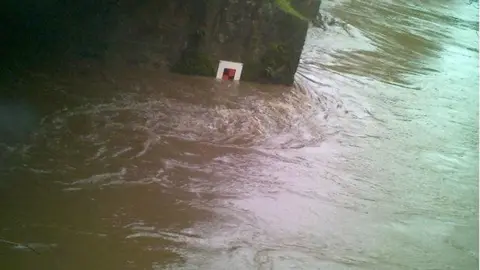 Network Rail Image showing flooding reaching the closure marker on the Barnstaple-Crediton railway line. The water is brown and murky. 
