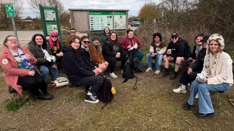 Megan Atkinson Group of around 20 people sat outside next to a nature reserve information board