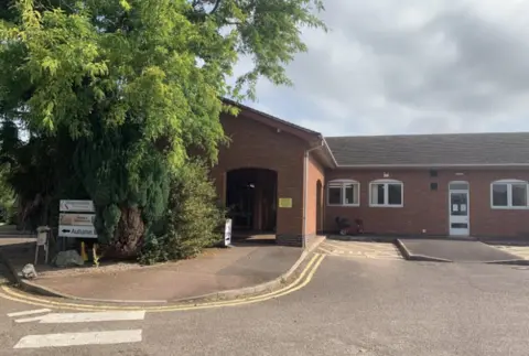 The former Roman Way Community Centre in Market Harborough. It is a red-bricked building on one level with a large tree to its right.