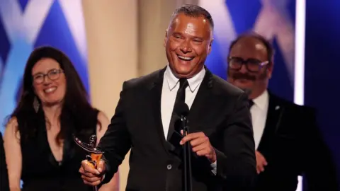 Getty Images Stan Grant holding an ACTAA award and speaking