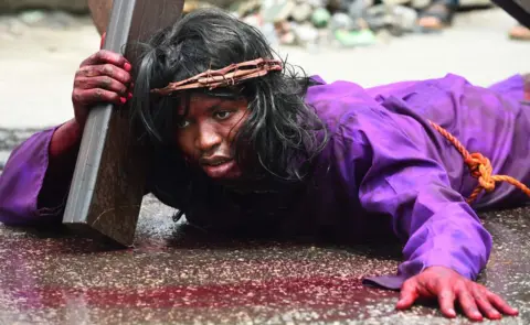 AFP A man lies on the ground carrying a crucifix during a dramatisation of the crucifixion of Jesus Christ to mark Good Friday, heralding the start of Easter celebrations, in Lagos on March 30, 2018.