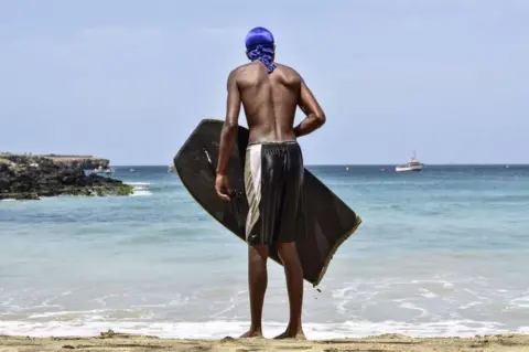 AFP A young man looks to the sea as he holds his bodyboard.