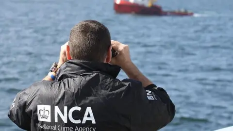 Getty Images An NCA officer watches as the MV Hamal was intercepted by the frigate HMS Somerset and Border Force cutter Valiant in 2015
