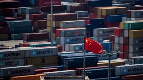 Getty Images A Chinese flag is seen in front of containers at the Yangshan Deep-Water Port, an automated cargo wharf, in Shanghai on April 9, 2018.