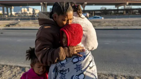 Getty Images Venezuelan immigrant Yaneisi Martinez weeps while embracing her three children after Texas National Guard troops and state police blocked a popular border crossing area on December 20, 2022 in Ciudad Juarez, Mexico