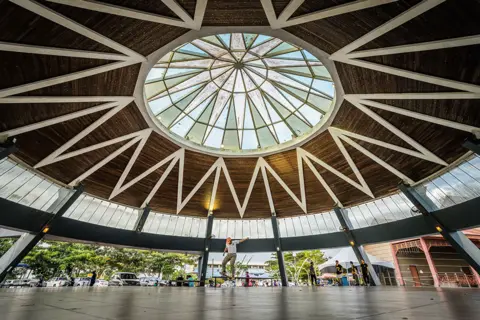 Desmond Chien Yew Ngu The large roof of a building in Kuching, Malaysia, with a skateboarder beneath