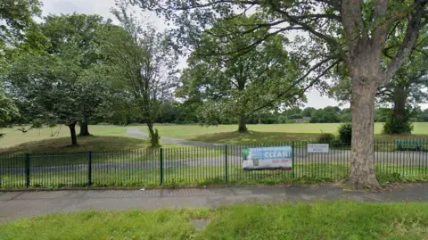 Google Firth Park in Sheffield, showing the gate, path and several large trees 