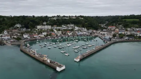 A small granite harbour at high tide, with boats in the harbour and a small village behind.