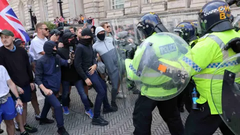 Reuters Protesters dressed in tracksuits, caps and face masks, clash with police in riot gear and holding shields outside Liverpool's Cunard building
