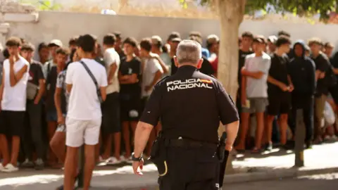 A police officer walks towards migrant children queuing outside a police station in Ceuta to be registered following mass crossings by migrants on foot and by sea from Morocco.