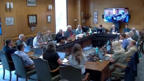 Local Democracy Reporting Service Male and female councillors sitting around a table with laptops placed on their desks in front of them
