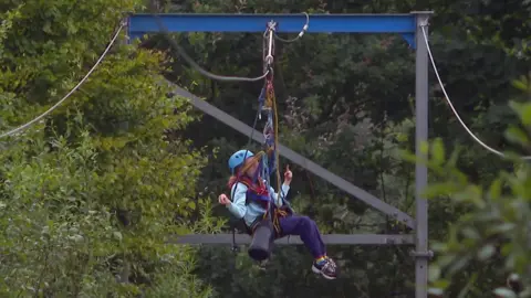 A person zipping down on a zip line with trees and woodland either side of them. 