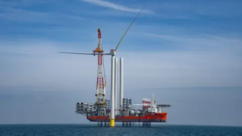 ScottishPower Renewables A wind turbine at sea, next to it is a platform being used as part of the construction process.