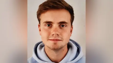  Avon and Somerset Police Photo of Jack who has brownish  hair, stubble, and is wearing a airy  bluish  hoodie.