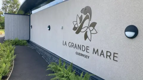 BBC An image of the outside of La Grande Mare. There is the building's sign which includes the logo and club name as well as a pathway next to the building. 