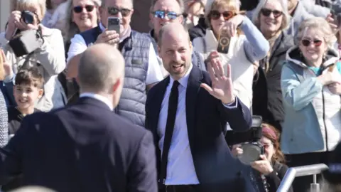 Prince of Wales waves to crowds of people surrounding him