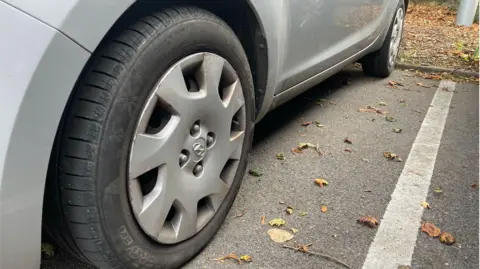 A picture of a car parked in a space. The image is zoomed in on the front tyre of the vehicle.