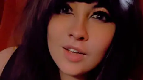 Lilly, a girl with dark hair and heavy eye make up is looking at the camera