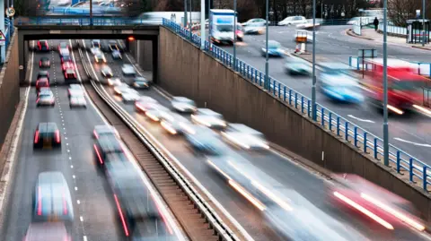 An aerial photo of a busy dual carriageway with lines of cars blurred by motion. 