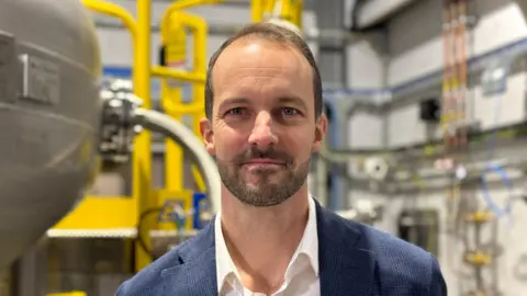 Levidian's CEO John Hartley wearing a blue suit and standing in front of the Loop system