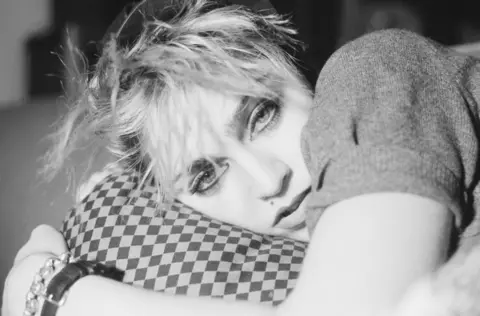 Getty Images A black and white promotional image of Madonna in 1982 shows the singer lying on a chequered pillow and gazing into the camera, while her artfully messy hair shows dark roots under bleached blonde tips