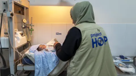 Project HOPE A midwife tending to a small baby on a bed in a medical setting