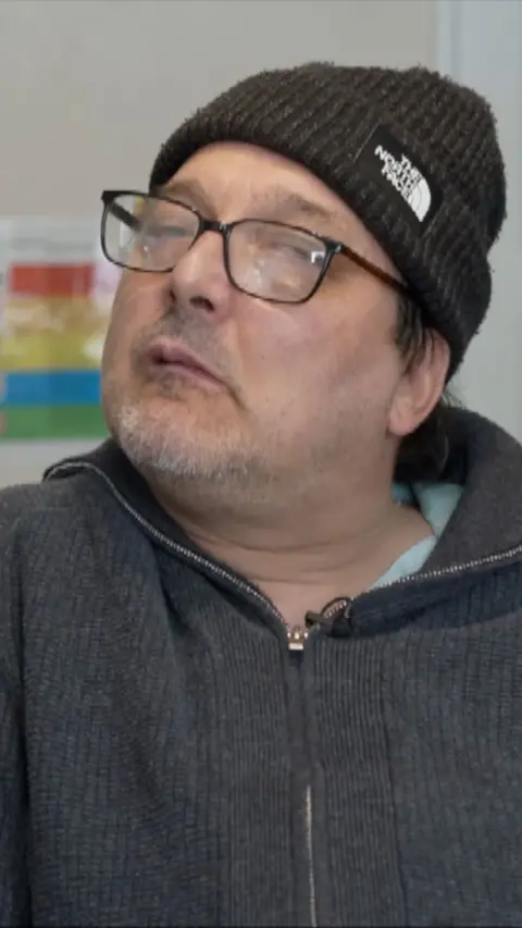 Head and shoulders image of man wearing black hat and fleece. He also has glasses on.