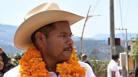 Photo showing Abino Gómez on the campaign trail wearing a flower garland