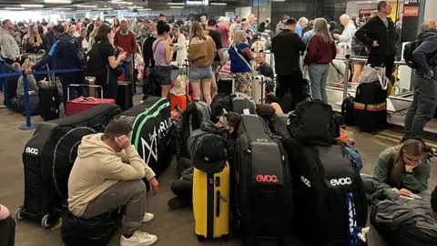 Reuters Passengers waiting in queues and sitting on the floor or on luggage outside Terminal 1 at Manchester Airport