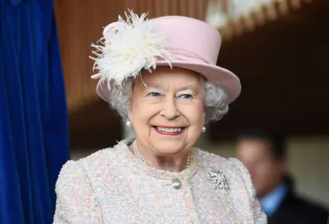Queen Elizabeth II in a pink hat smiling during an appearance