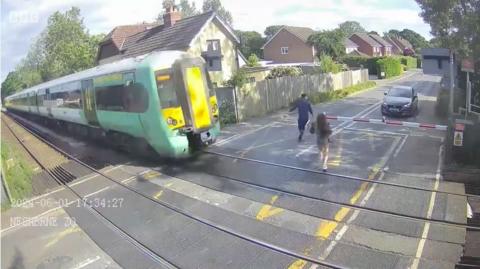 A young girl runs across a level crossing with a train coming towards her