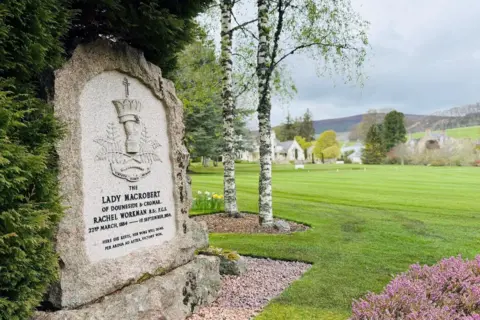 Stone tribute to Lady Rachel MacRobert, in a countryside setting, with words '22nd March 1884 - 1st September 1954', and 'Here she rests, her work well done'.