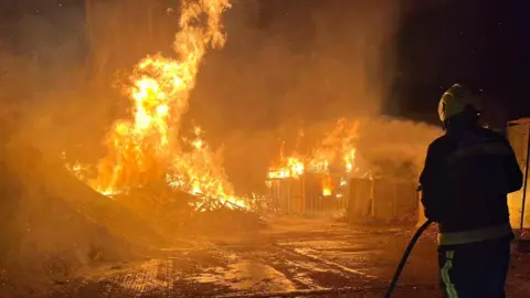 Taunton Fire Station A firefighter working to extinguish a large fire in Henlade, Somerset. The silhouette of the firefighter can be seen at the edge of the frame. 