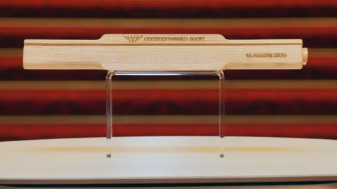 PA Media The wooden baton sitting on a plinth. It has the words Commonwealth Sport and Glasgow 2026 carved into it