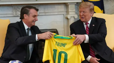 Getty Images Bolsonaro hands Trump a Brazil football shirt, with Trump's name on it, in the White House.