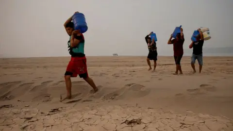 A group of four river dwellers carry water on a dried up river bed during a drought in Brazil