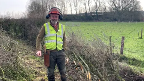 Bristol Water Mike Reed is standing in a field wearing a yellow high-vis vest and a helmet.