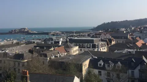 A view over the rooftops of St Peter Port. Showing various different buildings. Castle cornet is in the distance as is the marina. 