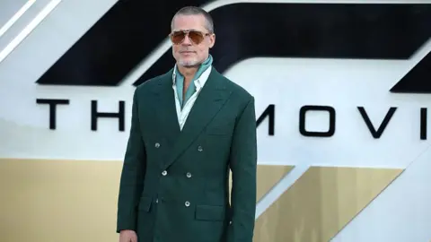 Actor Brad Pitt appears on the red carpet for his new movie F1. He is wearing a dark green suit with sunglasses