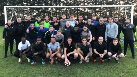 Jonathan Park/BBC The Great Wakering Rovers squad pose in front of a goal